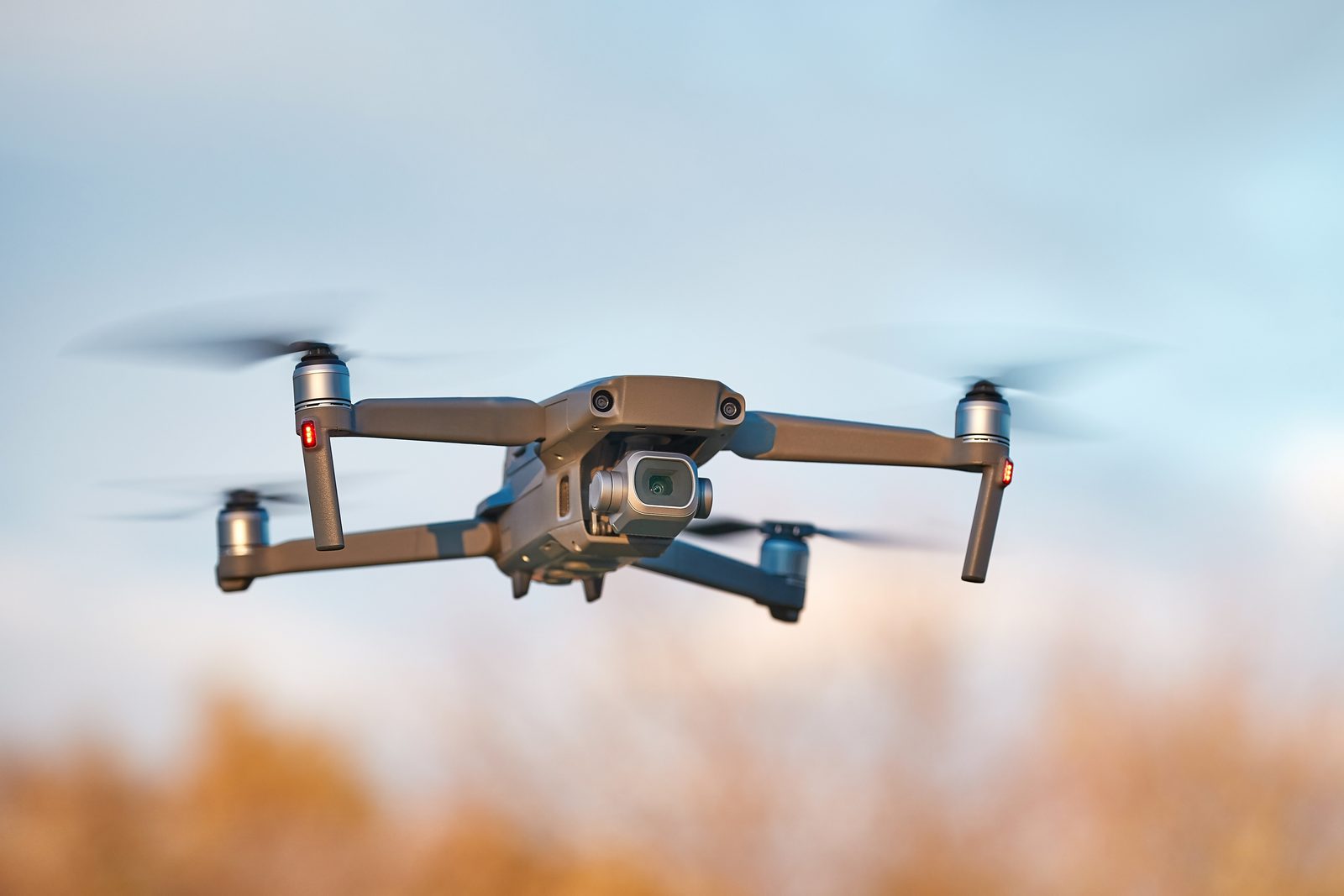 DJI drone in flight against a blue sky with autumn foliage below